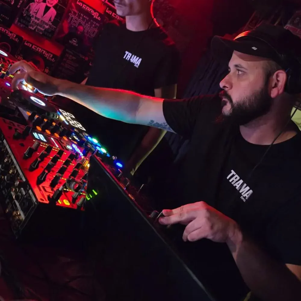 DJ local mezclando música techno en Pub La Canya, Benissa, con público animado y luces tenues.